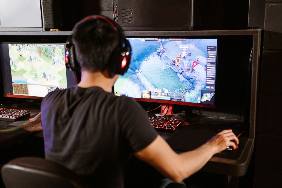 Adult male gamer immersed in PC gaming on dual monitors with headphones indoors.
